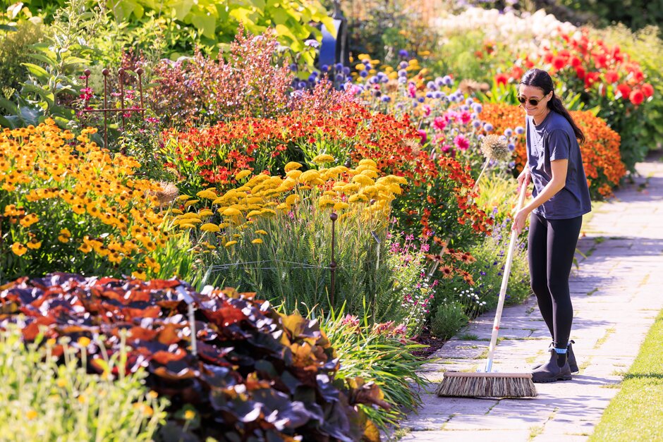 An RHS horticulturist is sweeping the paths of a garden.