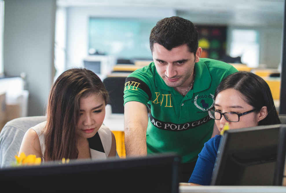 a guy teaching two students sitting at a table with laptops