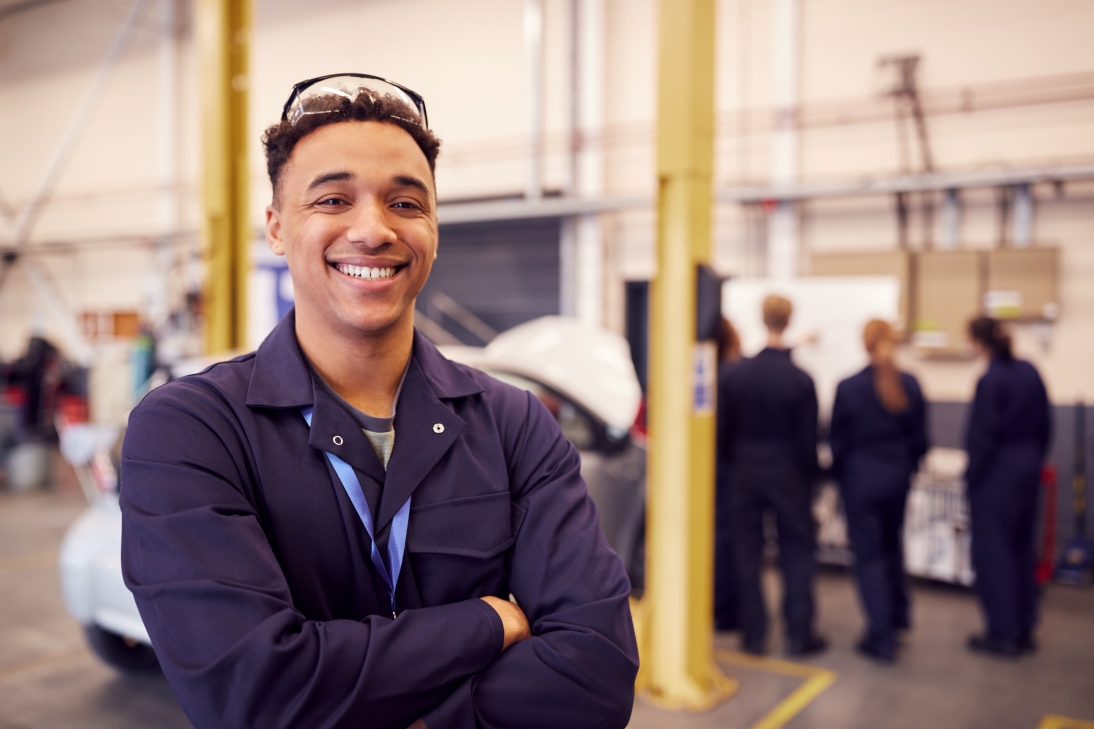 A young apprentice smiling at the camera with a group of peers behind him