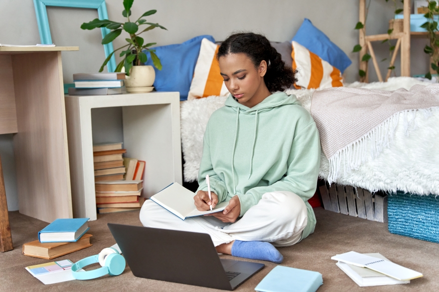 results day image 2 A young woman sitting next to her bed with her laptop and paper surrounding her.