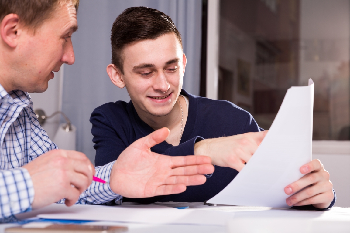 A young person with his father or guardian pointing at a piece of paper