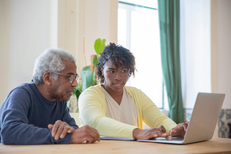 Woman-showing-man-how-to-use-computer A younger woman sat next to an older man showing him how to use a computer