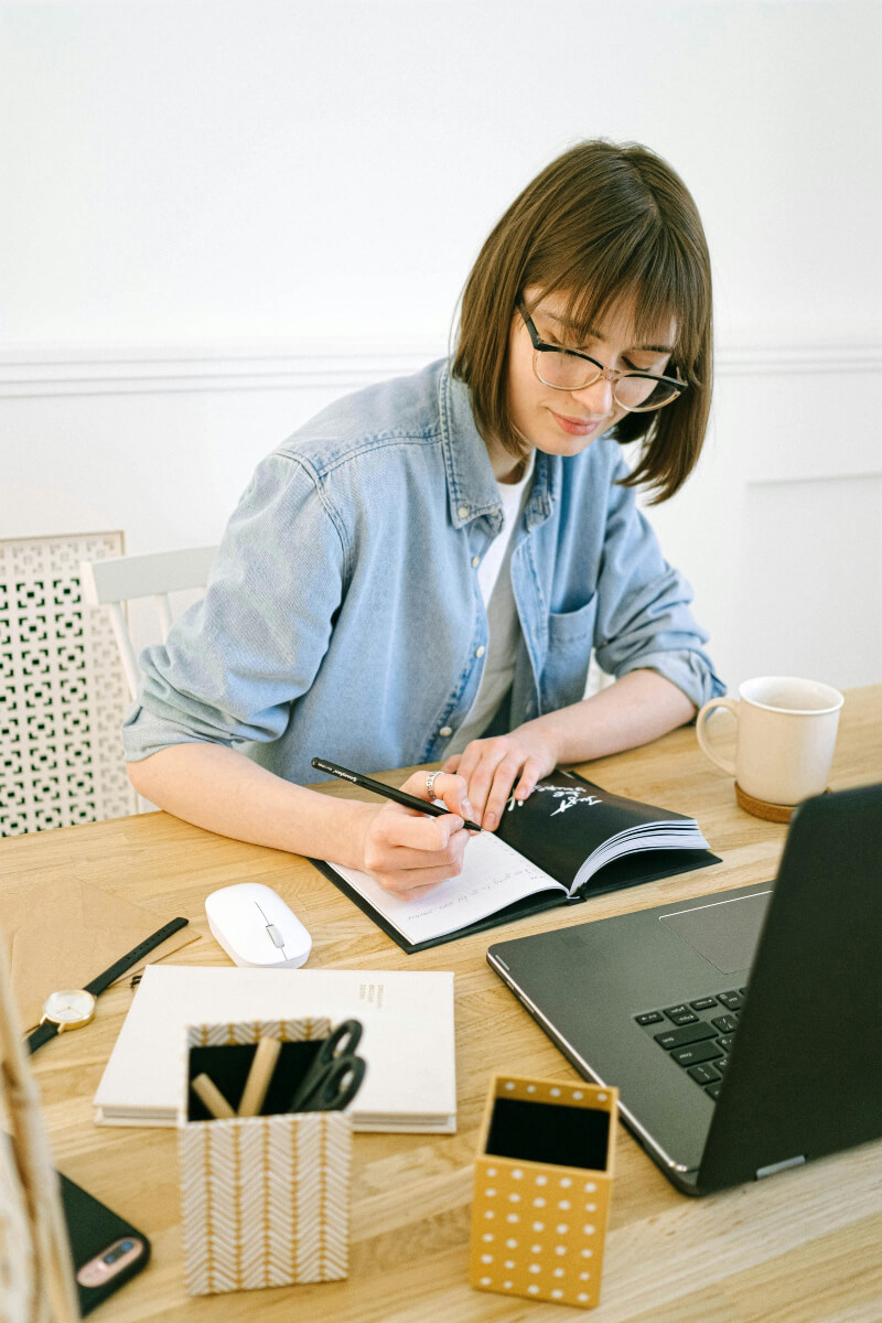 Woman Writing in Notebook with items on her desk.