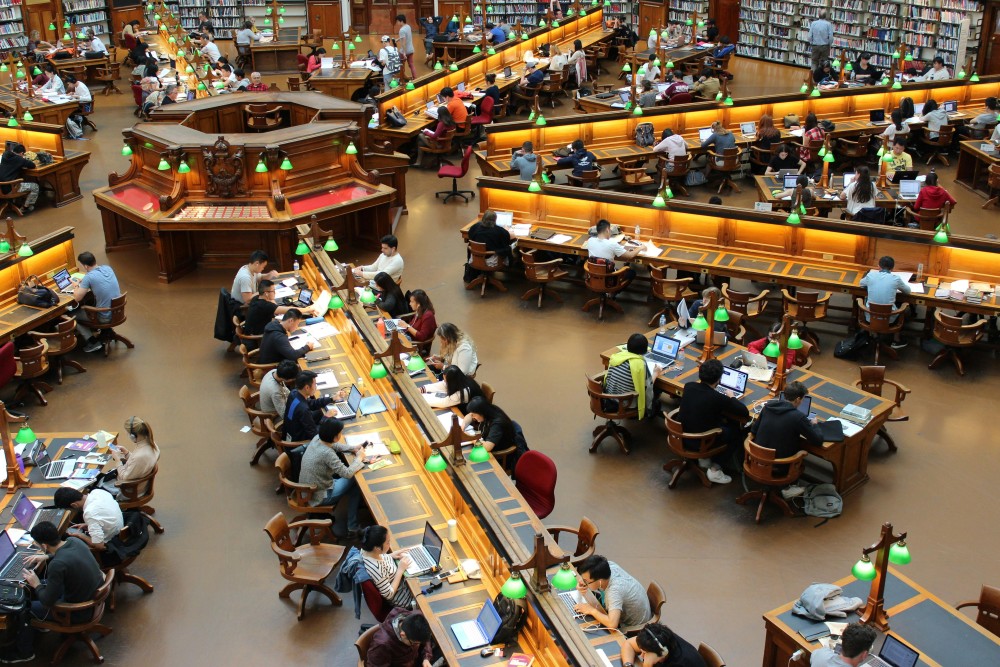 An overhead shot of a busy academic library with lots of students sitting at desks.