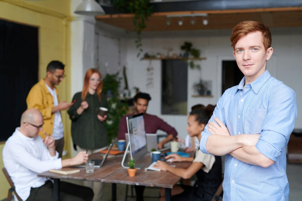 what are t levels placement image A young person with arms folded looking at the camera, in front of a table of work colleagues gathered around a laptop.
